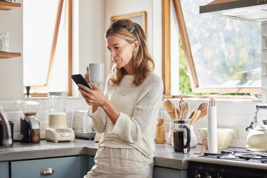 A woman drinking a coffee while looking at her phone.