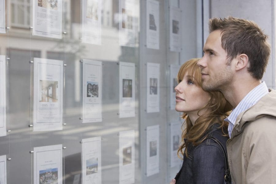 A couple looking at homes for sale in the window of an estate agent.