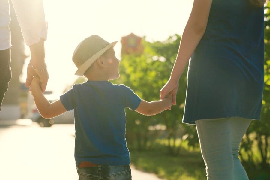 A family with a young child holding hands outdoors.