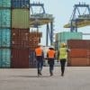Workers walking through a shipping cargo container terminal depot.