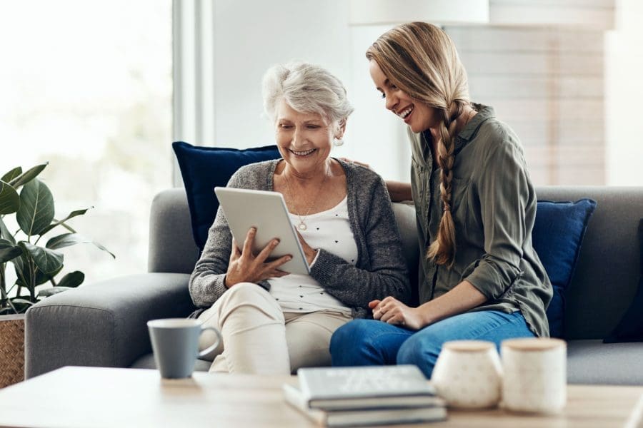 A woman showing her adult daughter something on a tablet.