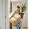 A woman carrying a box and a plant into her new home.