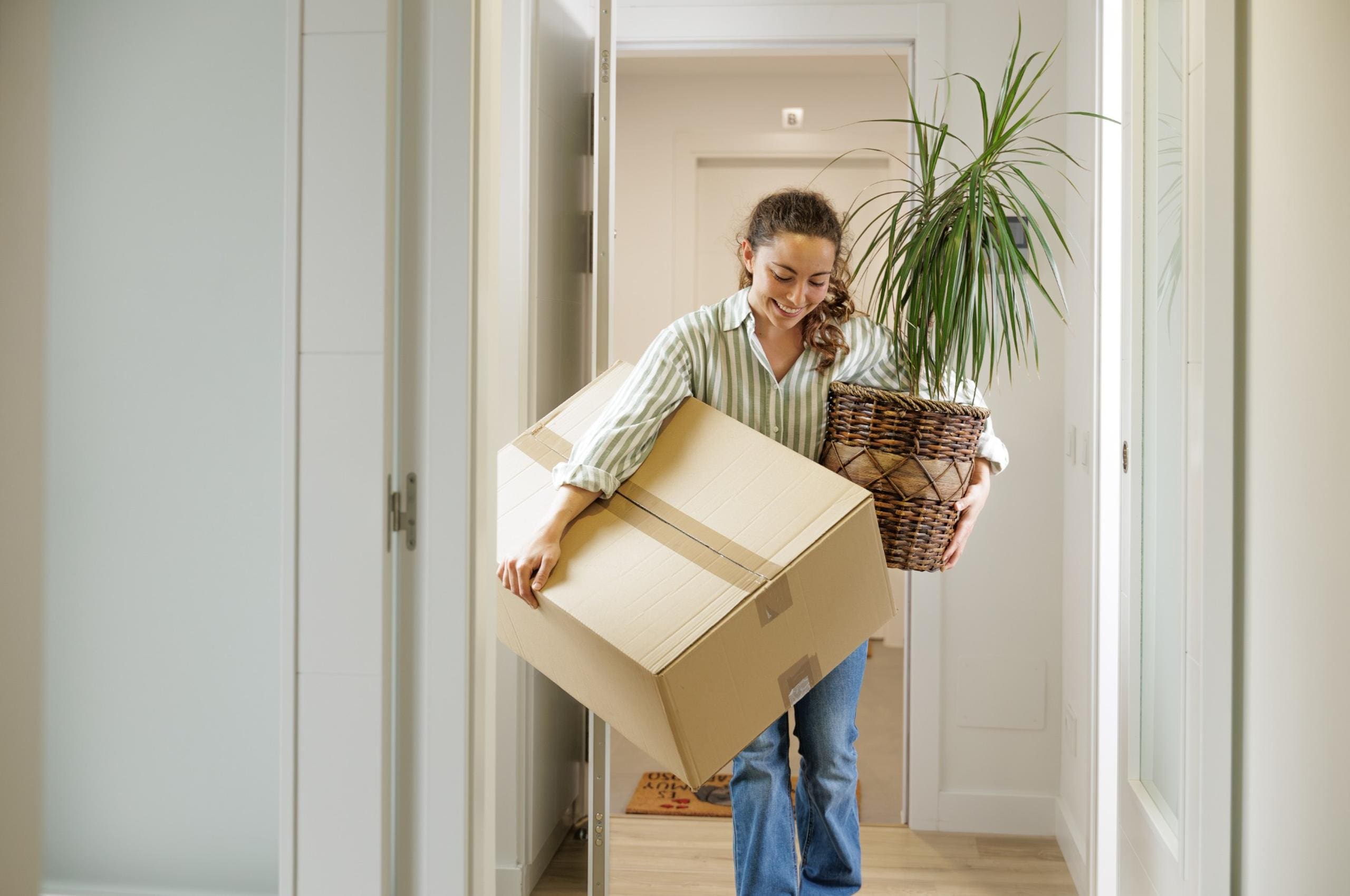 A woman carrying a box and a plant into her new home.